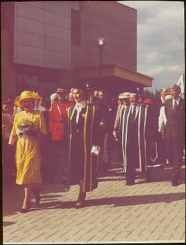Queen Elizabeth II, Chancellor Iona Campagnolo, and President Geoffrey R. Weller walk through a crowd in front of the Geoffrey R. Weller Library, UNBC