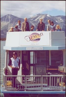 Chancellor's Tour - Iona Campagnolo stands with group on upper deck of the 'Theresa' houseboat in Atlin, BC