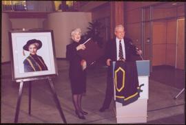 Chancellor's Farewell  - Iona Campagnolo standing with large book and roses, next to her portrait