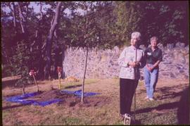 Iona Campagnolo holds shovel by an unidentified woman in front of newly planted tree