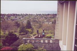 Distance view of three unidentified gardeners working behind Government House, with a view of Victoria and the ocean in background