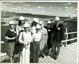Group photo of unidentified women and men posing on a wooden platform overlooking James Bay, all wearing hardhats