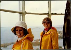 Two unidentified women in rain jackets at a window overlooking the ocean