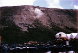 Tent camp with lumber and steel drums by mountain