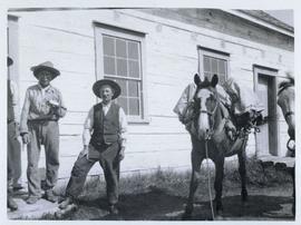 Two men and a pack horse standing in front of a building