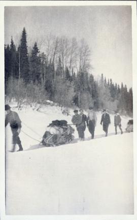 Several men towing their gear on sleds