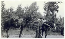 Man smoking pipe while holding a riding horse and a pack horse by the reins