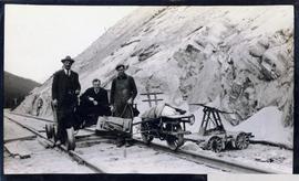 Three men standing next to a variety of rail carts