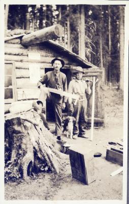 Two men with saws standing in front of a log cabin