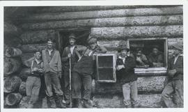 Several men standing in front of and in a log house