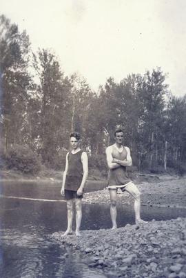 Two men in their bathing suits on the edge of a river
