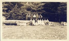 Several men and women seated on a log on the beach