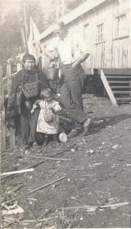 First Nations woman and child standing next to a man holding a bucket
