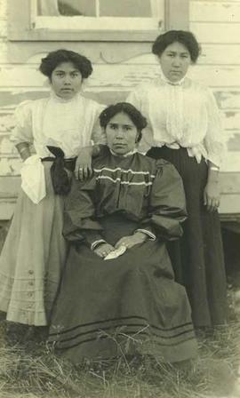Three First Nations women in front of a house