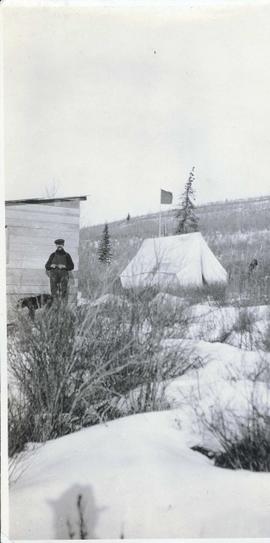 A man standing to the side of a tent in winter