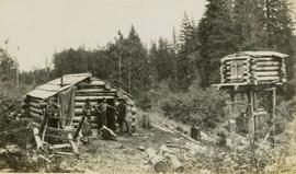 Log cabin and raised food cache with three men in yard