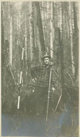 Surveyor posing with surveying equipment in front of trees