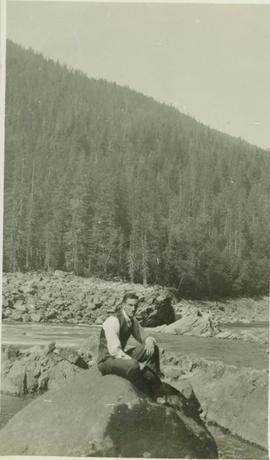 A man sitting on top of a rock next to a river