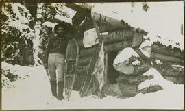 A man with snowshoes standing in front of a log cabin