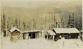 Homestead in winter with log cabin, wood shed, raised food cache, and two men in yard