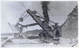 Steam shovel excavating and placing rubble into railcars