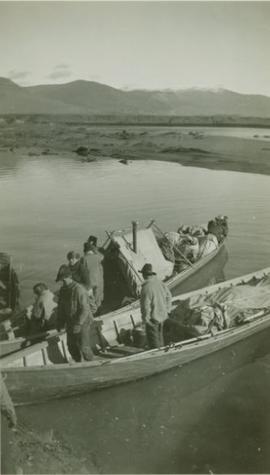 Men standing in supply laden canoes next to Pete Toy's bar