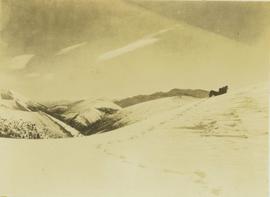 Guide laying on his back on a snow-covered mountain slope searching for game