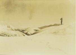 Guide standing on a snowy mountain peak searching for game through a pair of binoculars