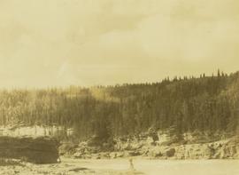 Two unidentified men standing along the rocky shores of the Peace River
