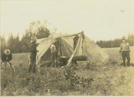 Five men setting up a tent on a grassy field