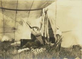 Harry Snyder sitting under a tent sighting his newly cleaned rifle