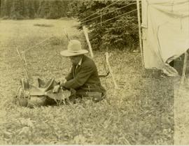 Pete Callao sitting on the ground near a tent fixing a saddle