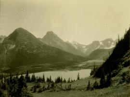 Forested valley with lake rising to snow capped mountain peaks 