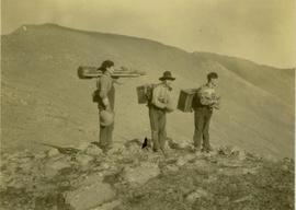 (L-R) Billy Taylor, Johnny Napolean and Pete Callao stand on a rocky mountain top carrying camera equipment