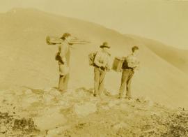 (L-R) Billy Taylor, Johnny Napolean and Pete Callao standing on a rocky mountain peak carrying camera equipment