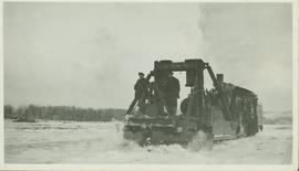 Two unidentified men standing on a railroad snow plow connected to the front of a train which is ...