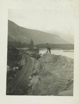 Man (R.A. Harlow?) standing on a large boulder overlooking a railway track