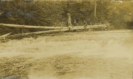 Unidentified man sitting on a felled tree which spans over a small waterfall