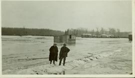 Two unidentified men standing on a snowy 'berm' in the flooded CNR yard at Prince George