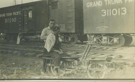 Unidentified man giving another man a haircut next to railway tracks